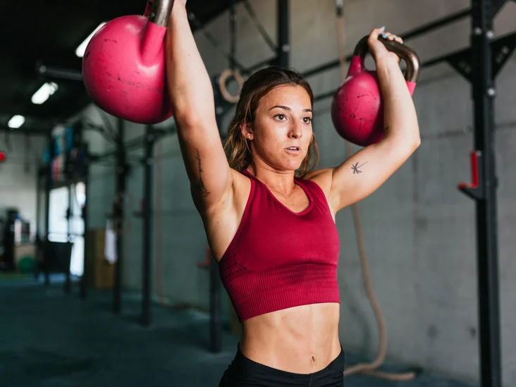 woman in red tank top lifting 2 kettlebells